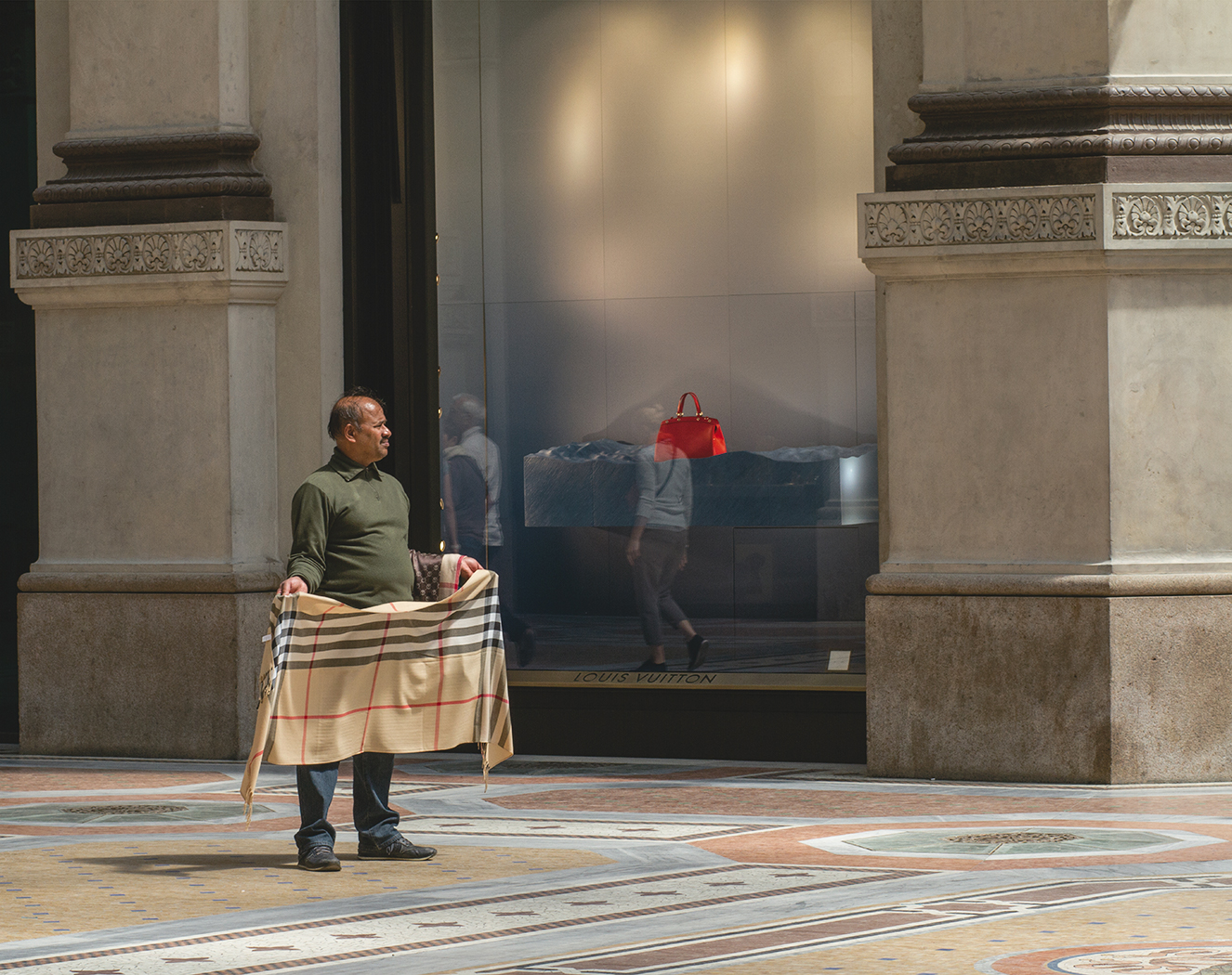 Milan.  Louis Vuitton in the window. A street seller with a shawl.